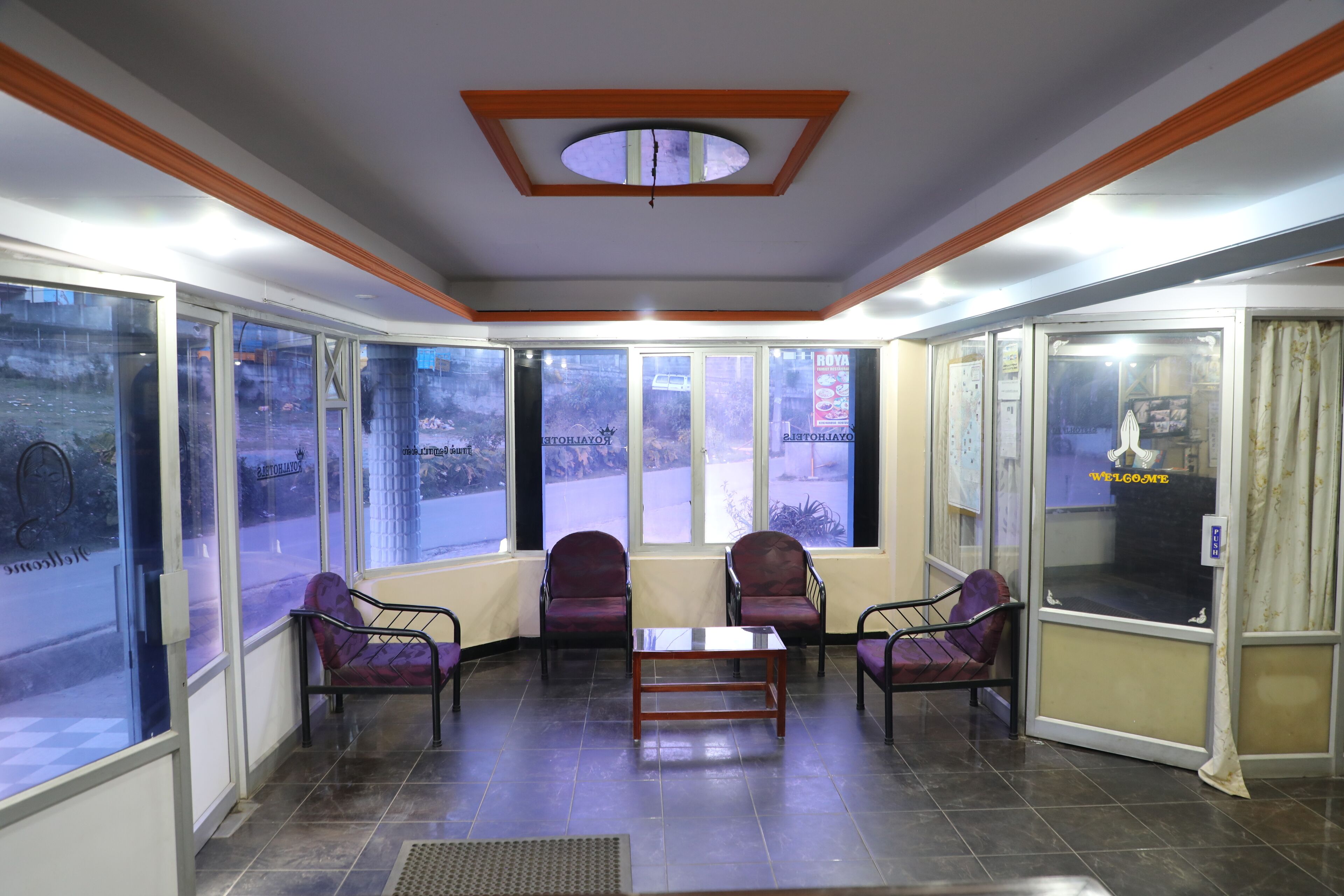 A waiting area with a glass wall, a ceiling with a wooden beam, and a table with chairs.