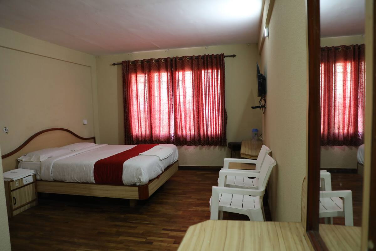 A hotel room with a bed, a desk, a chair, and a window with curtains.