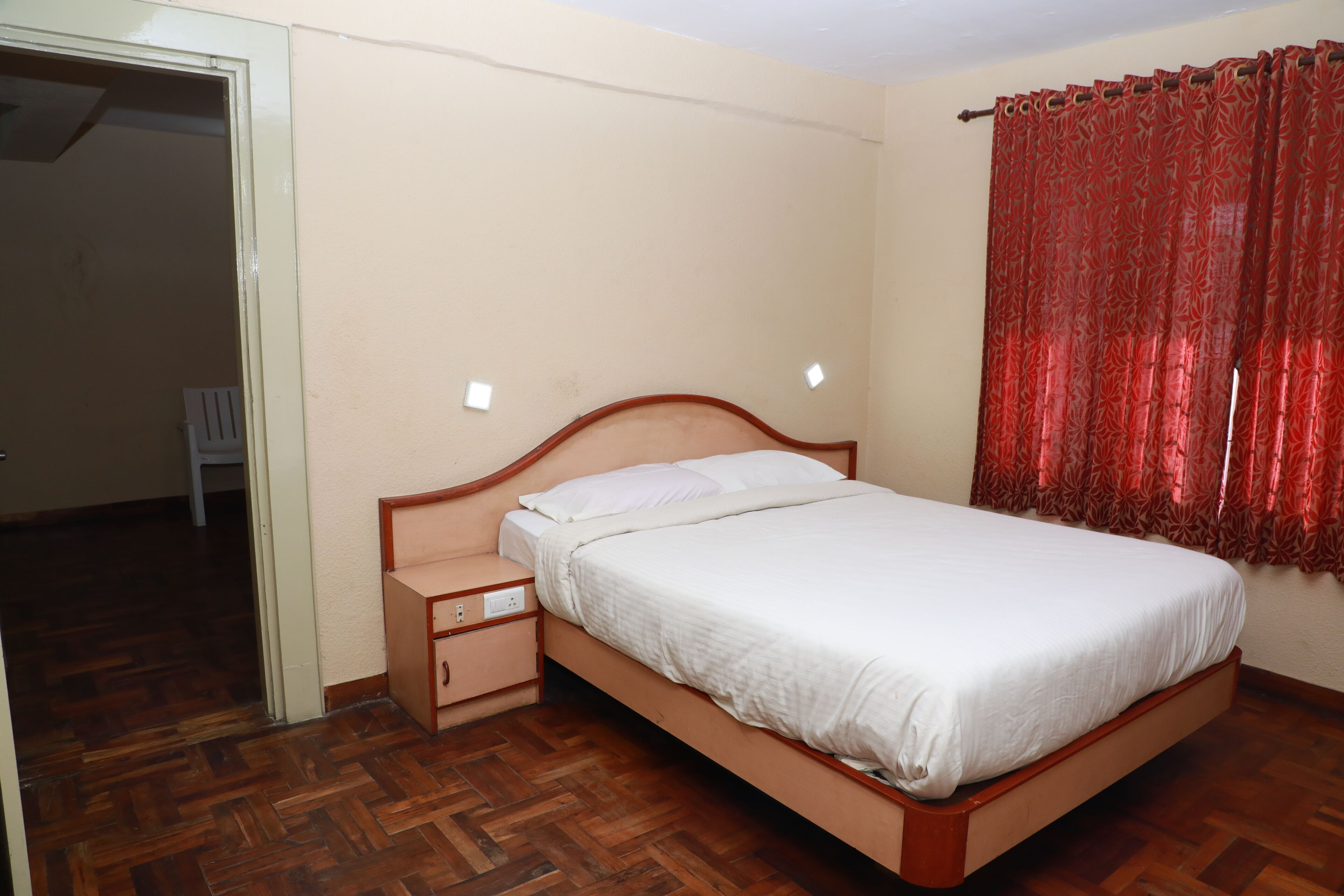 A bedroom with a wooden bed, a nightstand, a red curtain, and a wooden floor.