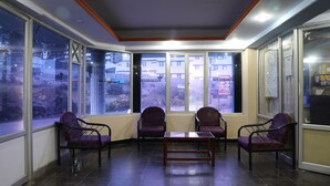 A reception area with large windows, a reception desk, and several chairs. - Royal Hotels, Kodaikanal (Kodaikanal)