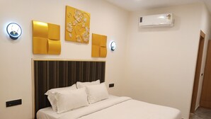 A bedroom with a bed, bedside tables, wall-mounted lights, and an air conditioner. - Hotel Indriya (Greater Noida)