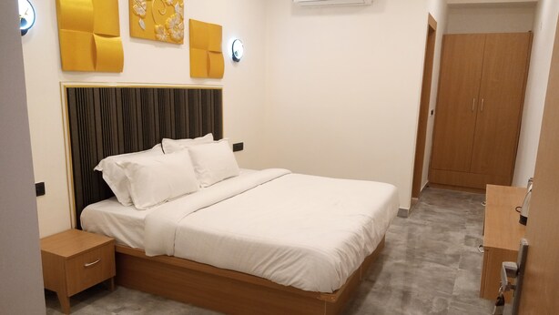 A neatly arranged bedroom with a bed, bedside tables, a wardrobe, and an air conditioning unit. - Hotel Indriya (Greater Noida)