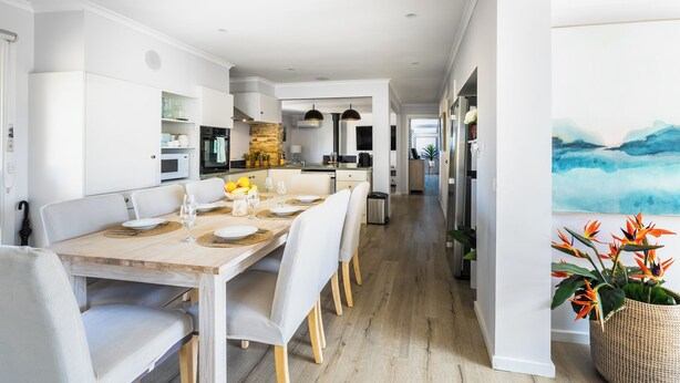 Une cuisine moderne avec des meubles blancs, une table à manger en bois pour quatre personnes et une vue sur la salle à manger adjacente.