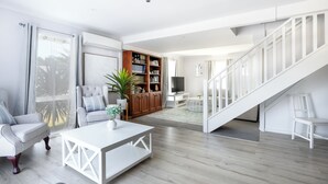 Un salon spacieux avec un escalier blanc, une bibliothèque et un coin salon confortable.