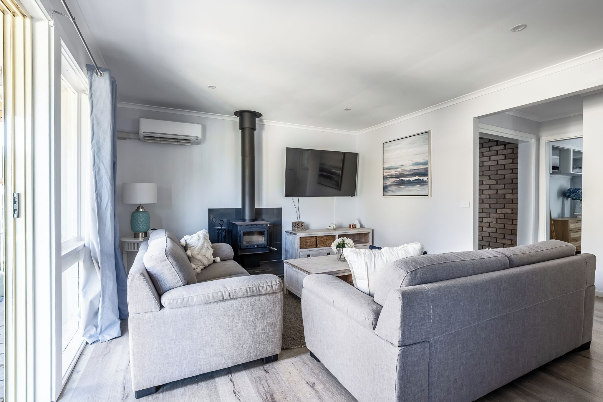 Ein modernes Wohnzimmer mit Kamin, grauen Sofas, einem Fernseher und Blick ins Freie.
