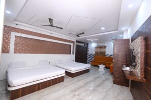A modern bedroom with two beds, a sofa, a desk, and a ceiling fan. - Kamala Hotel (Deoghar)