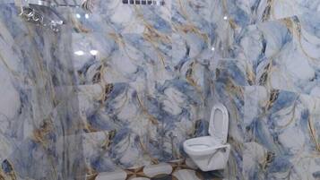 A bathroom with marble walls and a patterned floor, a toilet, and a red bucket.