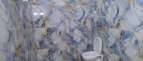 A bathroom with marble walls and a patterned floor, a toilet, and a red bucket.