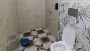 A bathroom with a toilet, shower, and patterned floor tiles. - Kamala Hotel (Deoghar)
