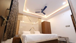 A modern bedroom with a bed, a ceiling fan, and a nightstand. - Kamala Hotel (Deoghar)