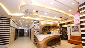 A hotel reception area with a curved reception desk, a man standing behind it, and a staircase leading to an upper level. - Kamala Hotel (Deoghar)