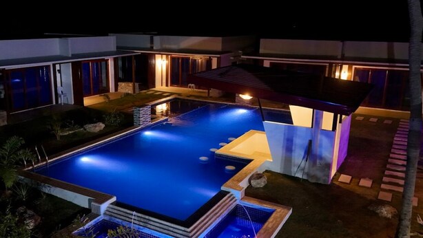 Ein modernes Haus mit Swimmingpool, überdachter Terrasse und einer gut beleuchteten Außenfassade bei Nacht.
