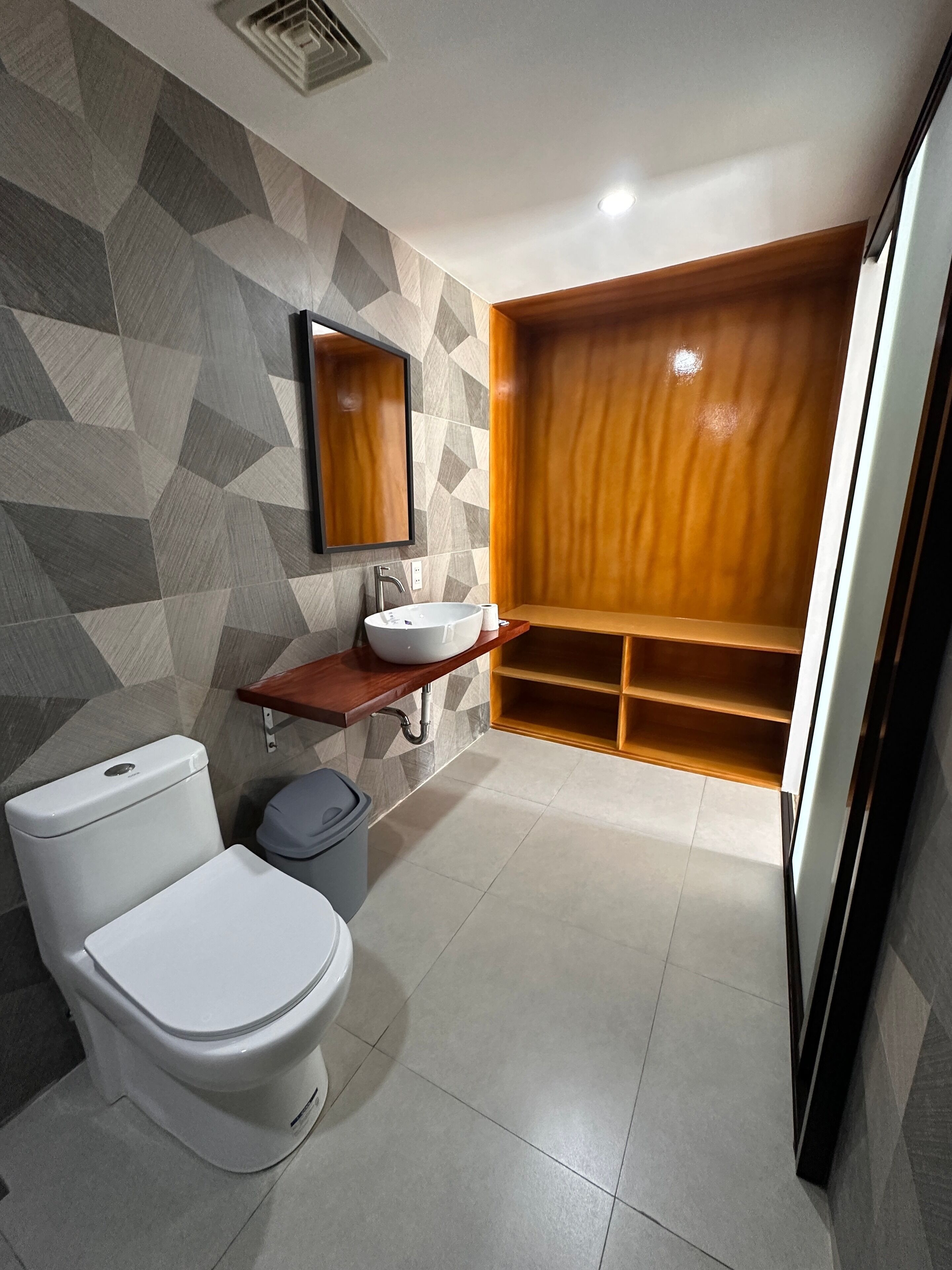 A modern bathroom with a geometric-patterned wall, a wooden vanity, a white sink, and a toilet.