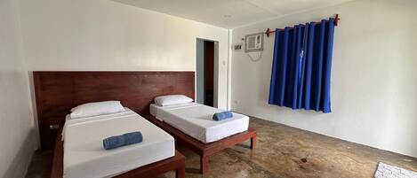 Habitación de hotel con dos camas individuales, cabecero de madera, cortina azul y una mesita.
