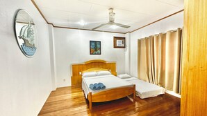 Ein Schlafzimmer mit einem hölzernen Bett, einem Deckenventilator, einer Wandklimaanlage und einem Fenster mit Vorhängen.