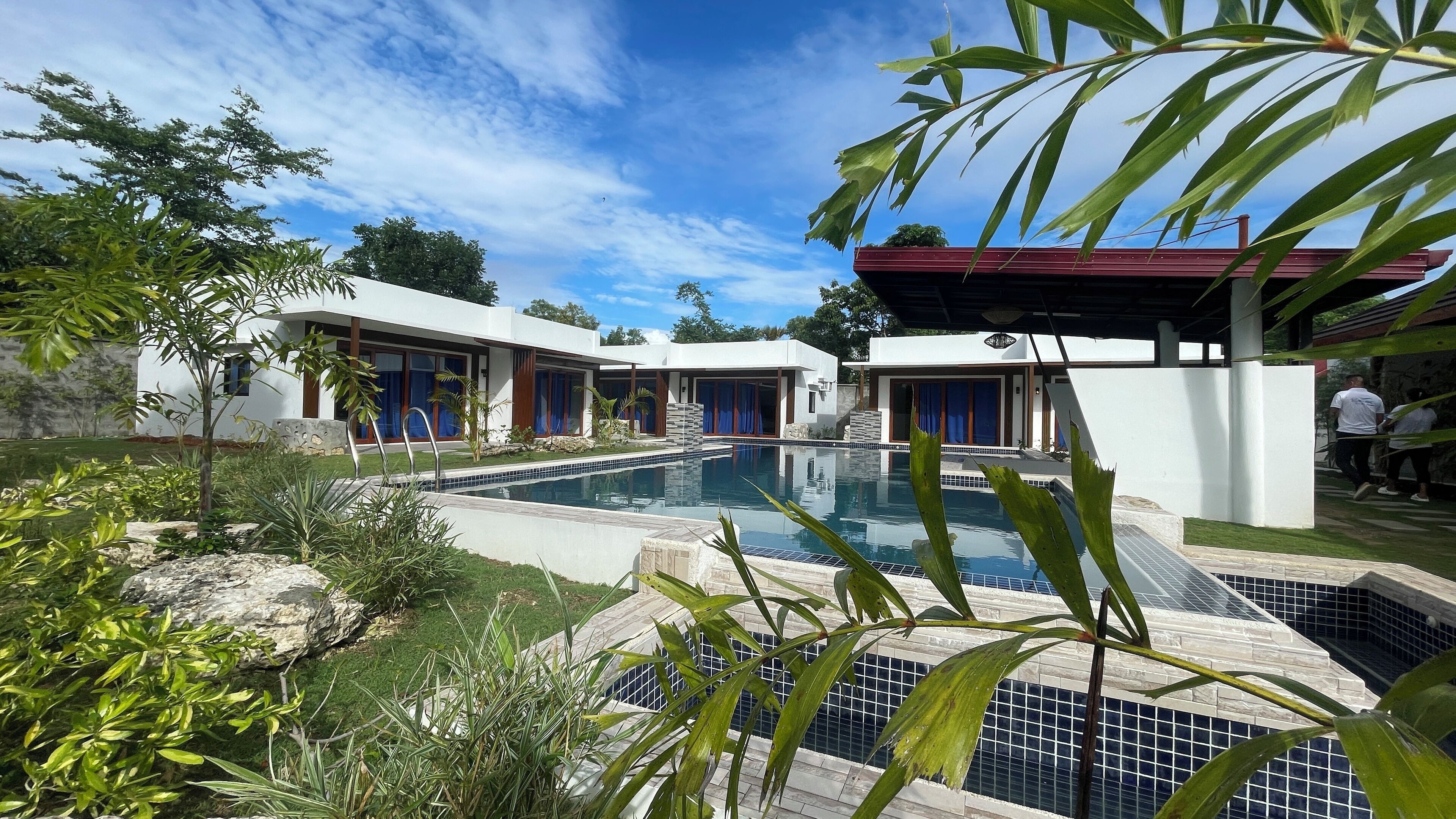 A modern pool area with a clear blue sky, surrounded by white buildings with large windows and a covered seating area.