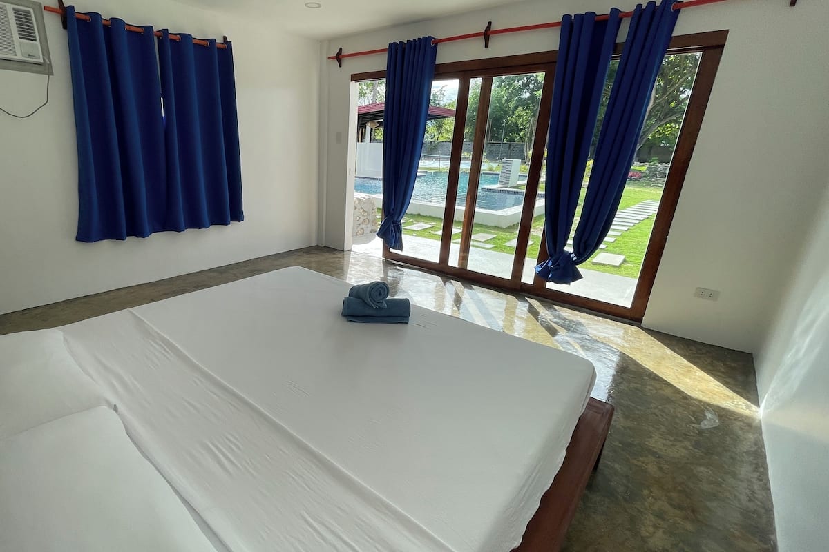 Una habitación de hotel con una cama grande, una ventana con cortinas azules y vistas a una piscina.