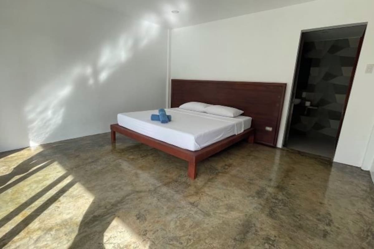 Une chambre à coucher avec un lit en bois, du linge de lit blanc et une porte ornée d’un motif géométrique.