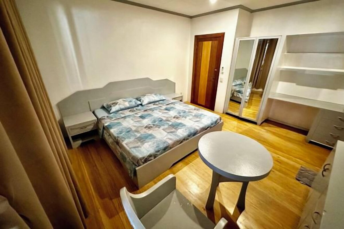 Un dormitorio con cama, una mesita, una silla, un armario y una puerta corrediza que da a otra habitación.