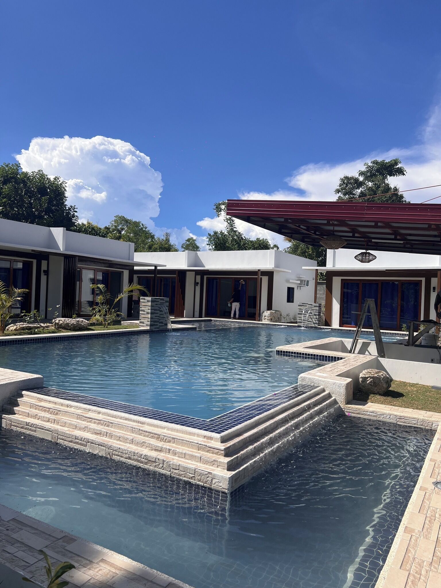A modern pool area with clear blue water, stone steps, and a covered seating area.