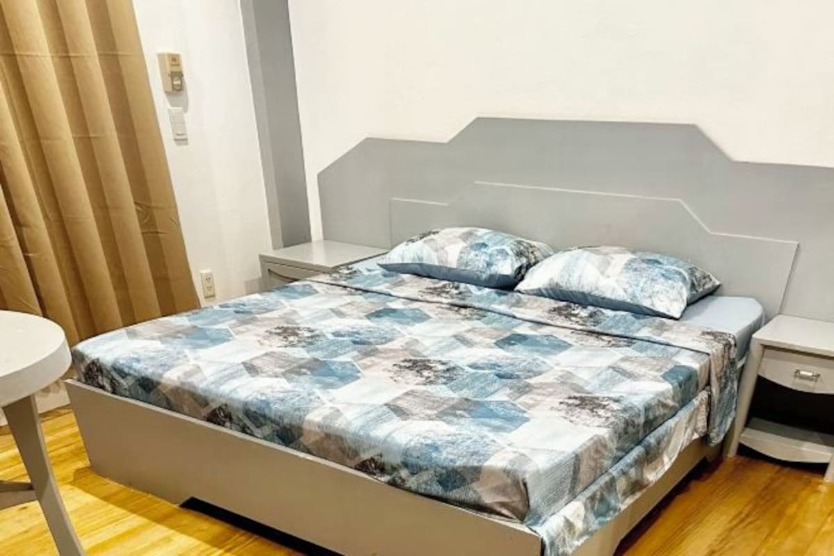 Une chambre à coucher avec un lit, deux tables de chevet, une petite table ronde et un rideau.