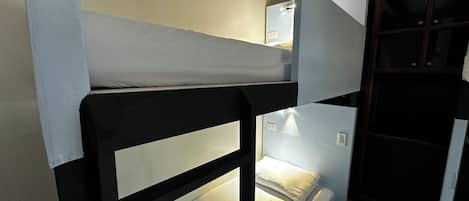 A bunk bed with a white mattress and a black frame. There is a small window above the top bunk.