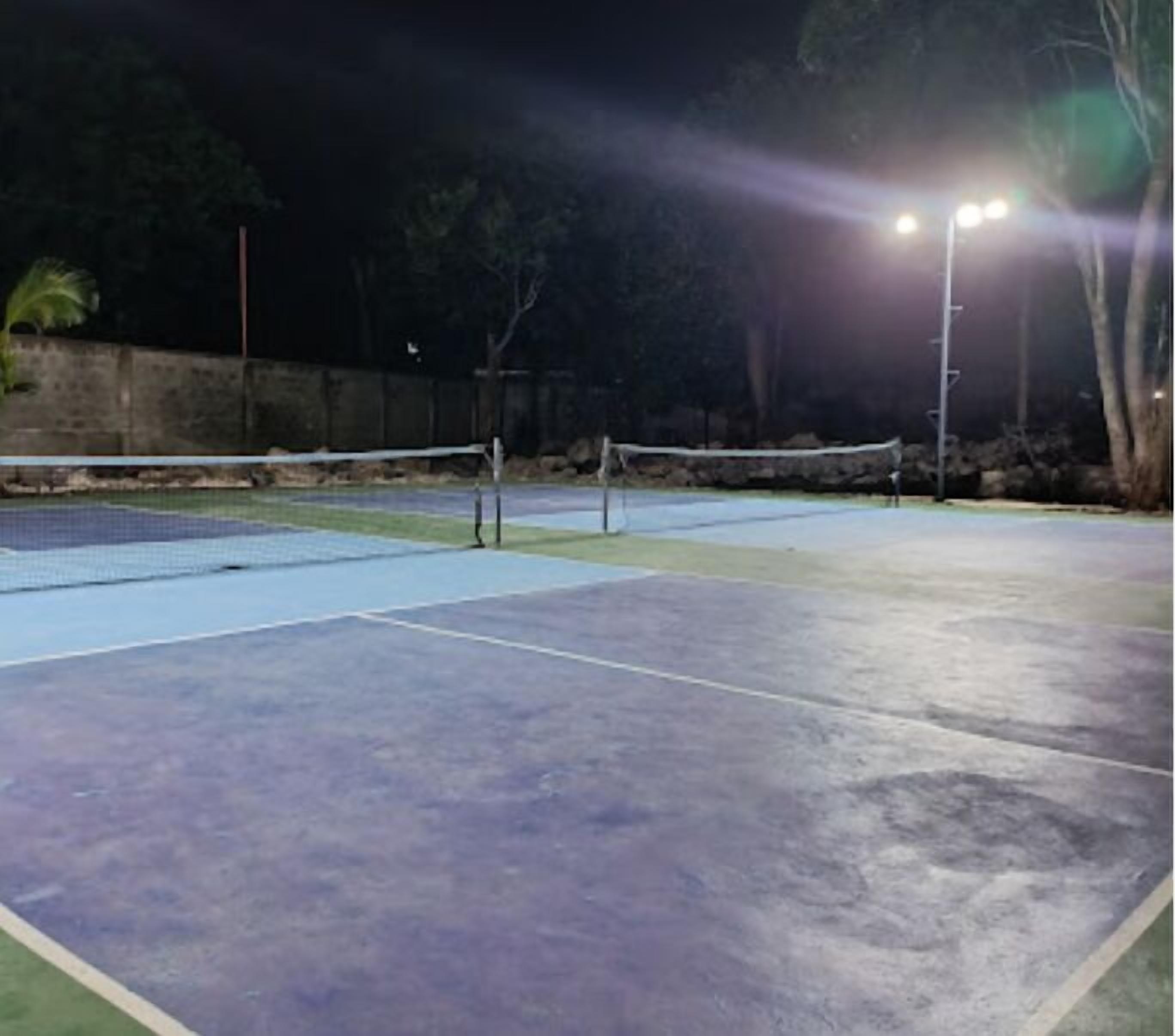An outdoor tennis court at night with floodlights.