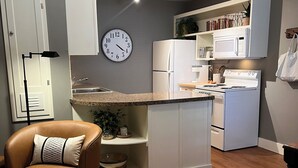 A modern kitchen with white appliances, a clock, and a brown leather chair.