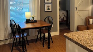A dining area with a wooden table and chairs, a window with blinds, a ceiling fan, and a door leading to another room.