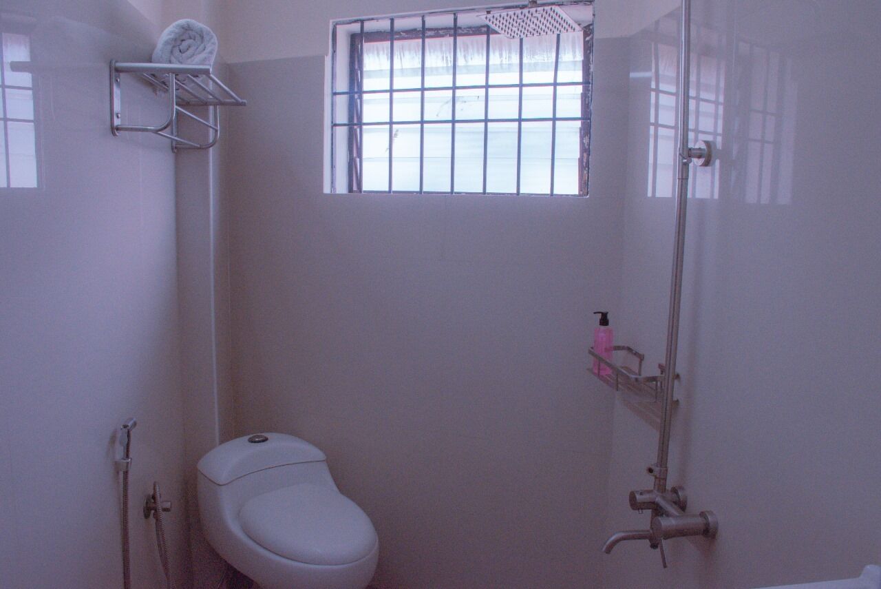 A small, white bathroom with a toilet, a shower, and a window with bars.