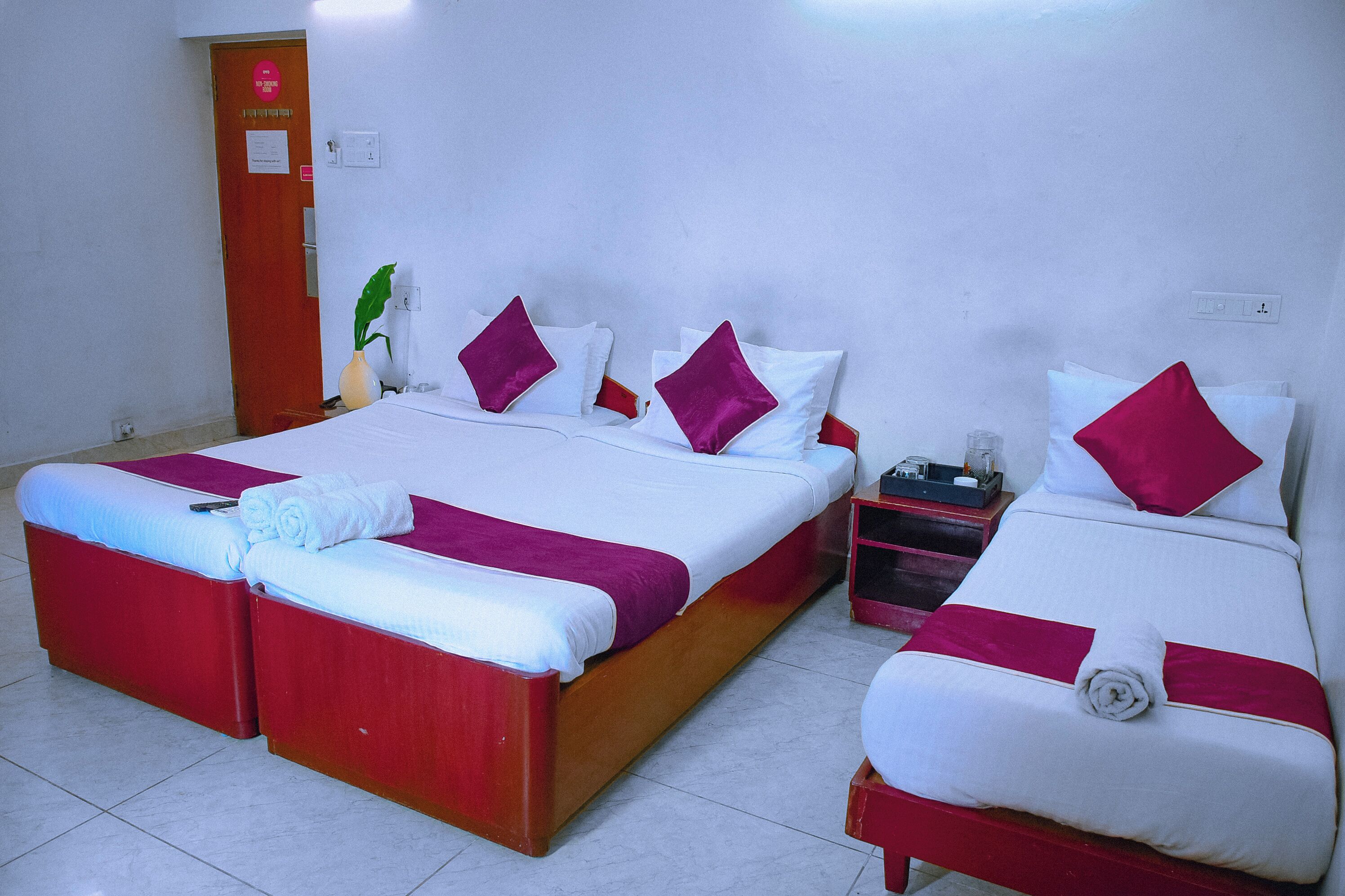 Una habitación de hotel con dos camas, cada una con ropa de cama blanca y detalles en rojo.