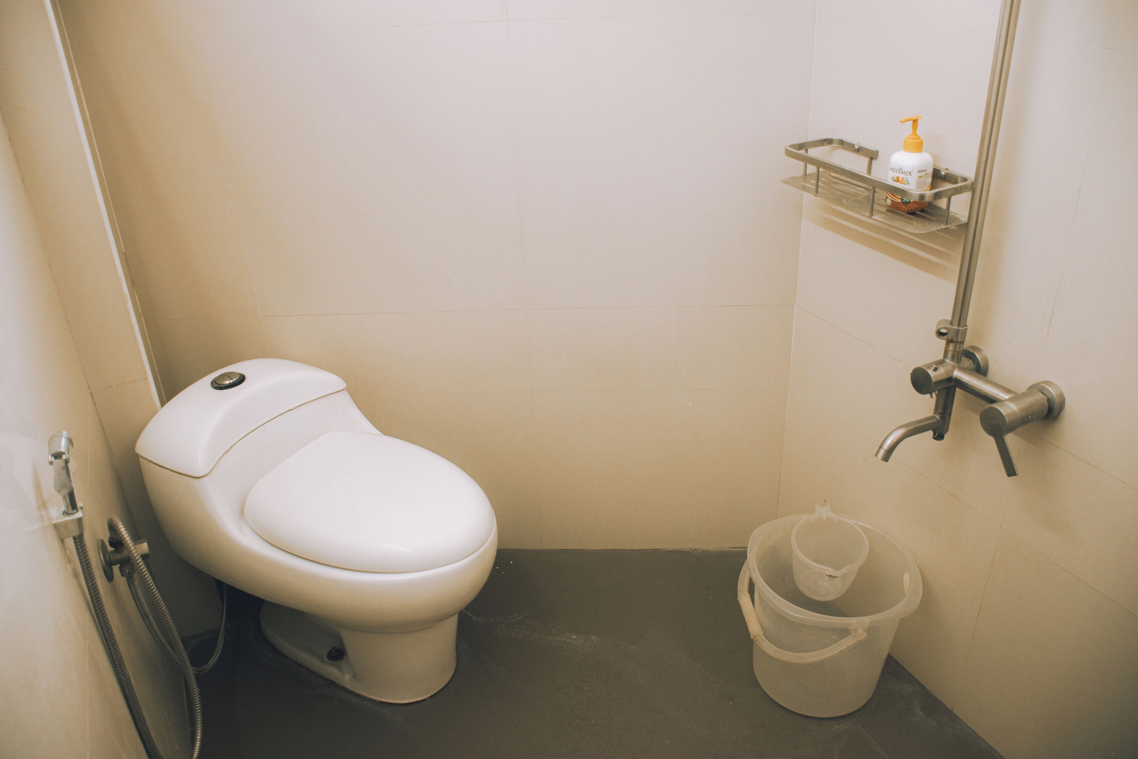 Un baño pequeño y limpio, con inodoro, ducha y un estante con artículos de aseo.