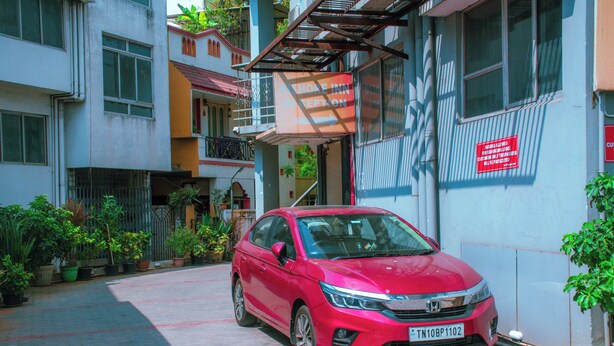 A red Honda car parked in front of a building with a sign indicating a reception area. - Naksha Tree Hotels Kishore Inn - Koyambedu (Chennai)