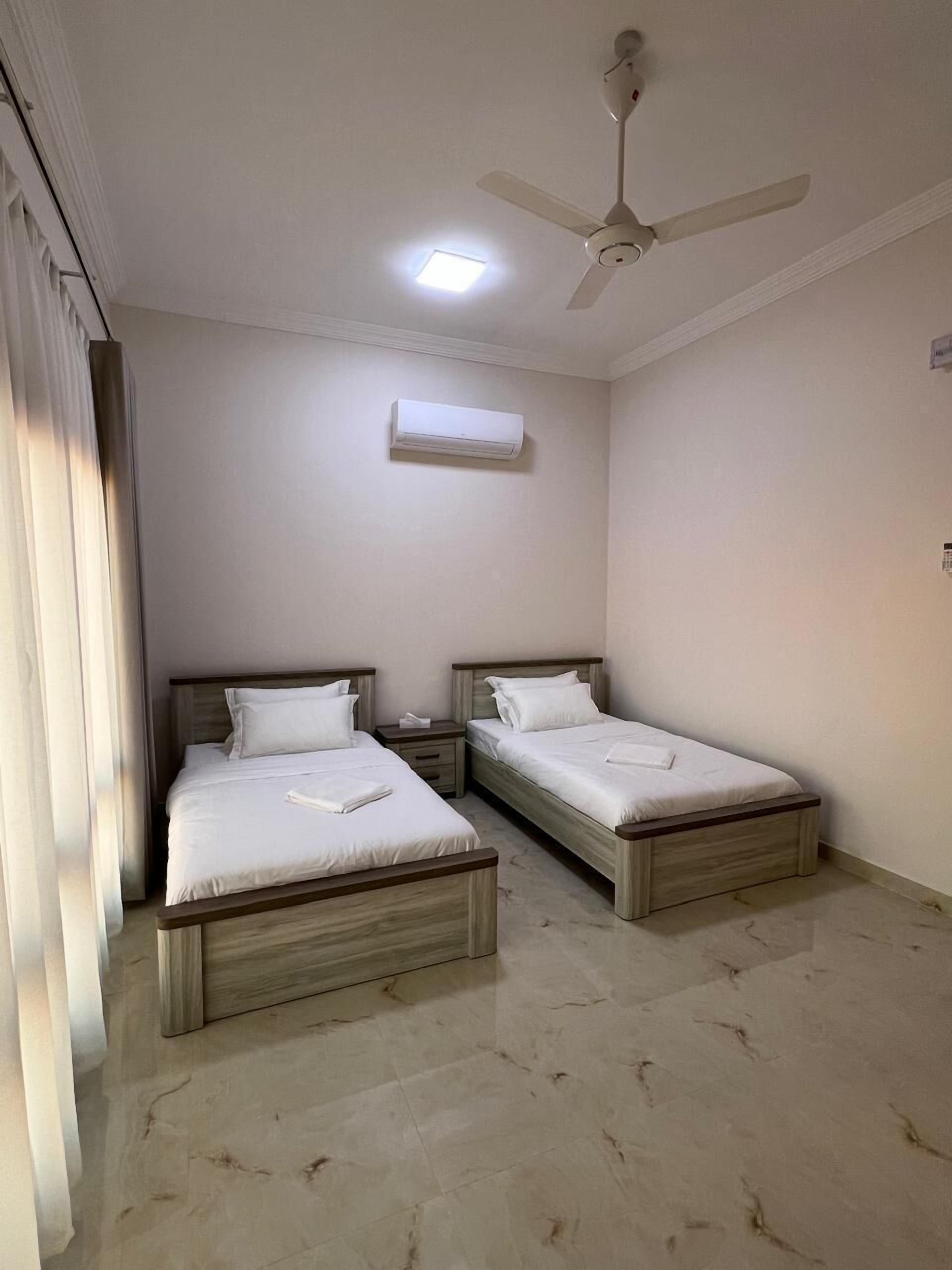 A hotel room with two single beds, a ceiling fan, an air conditioning unit, and a small window.