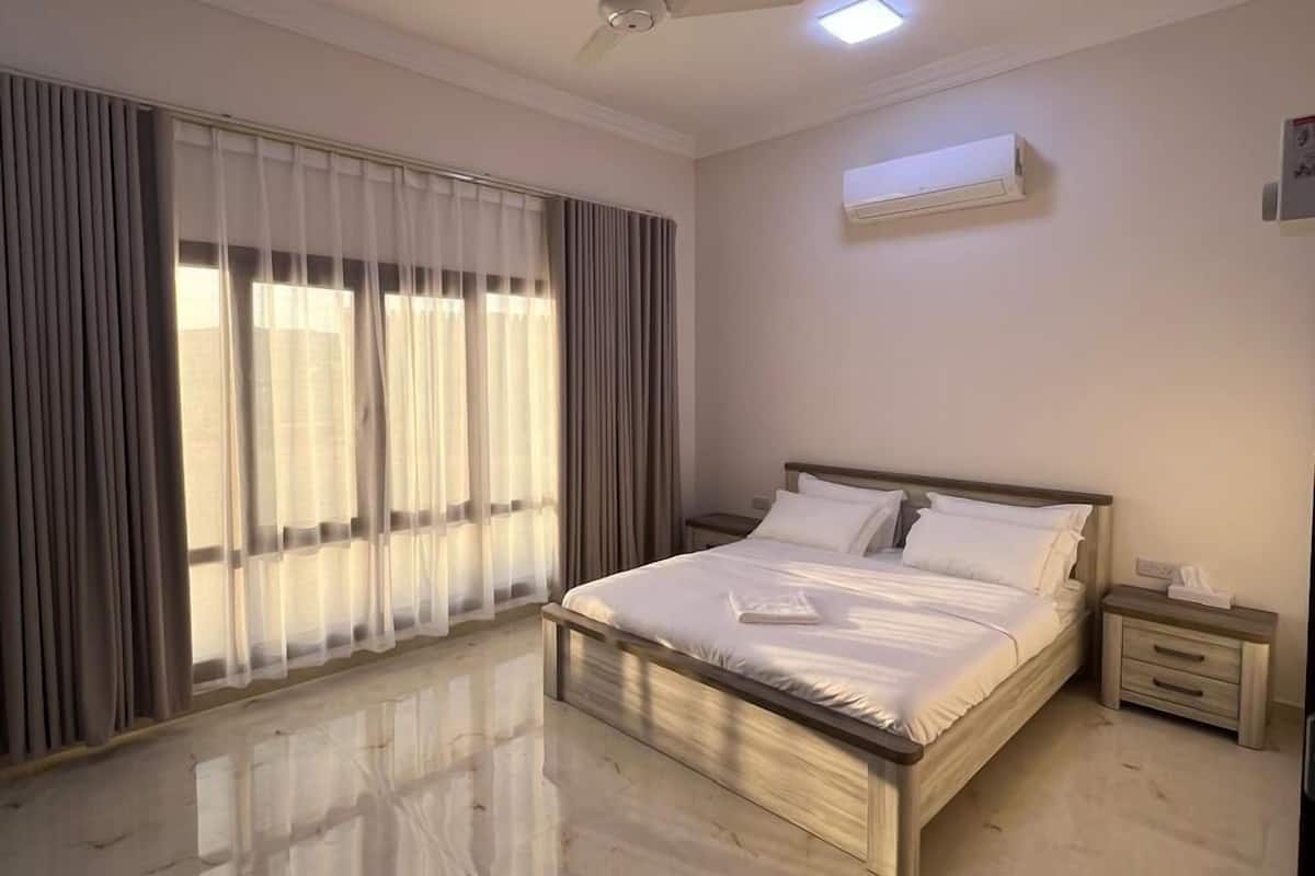 A bedroom with a bed, a ceiling fan, an air conditioning unit, and a nightstand.