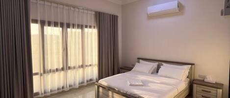 A bedroom with a bed, a ceiling fan, an air conditioning unit, and a nightstand.