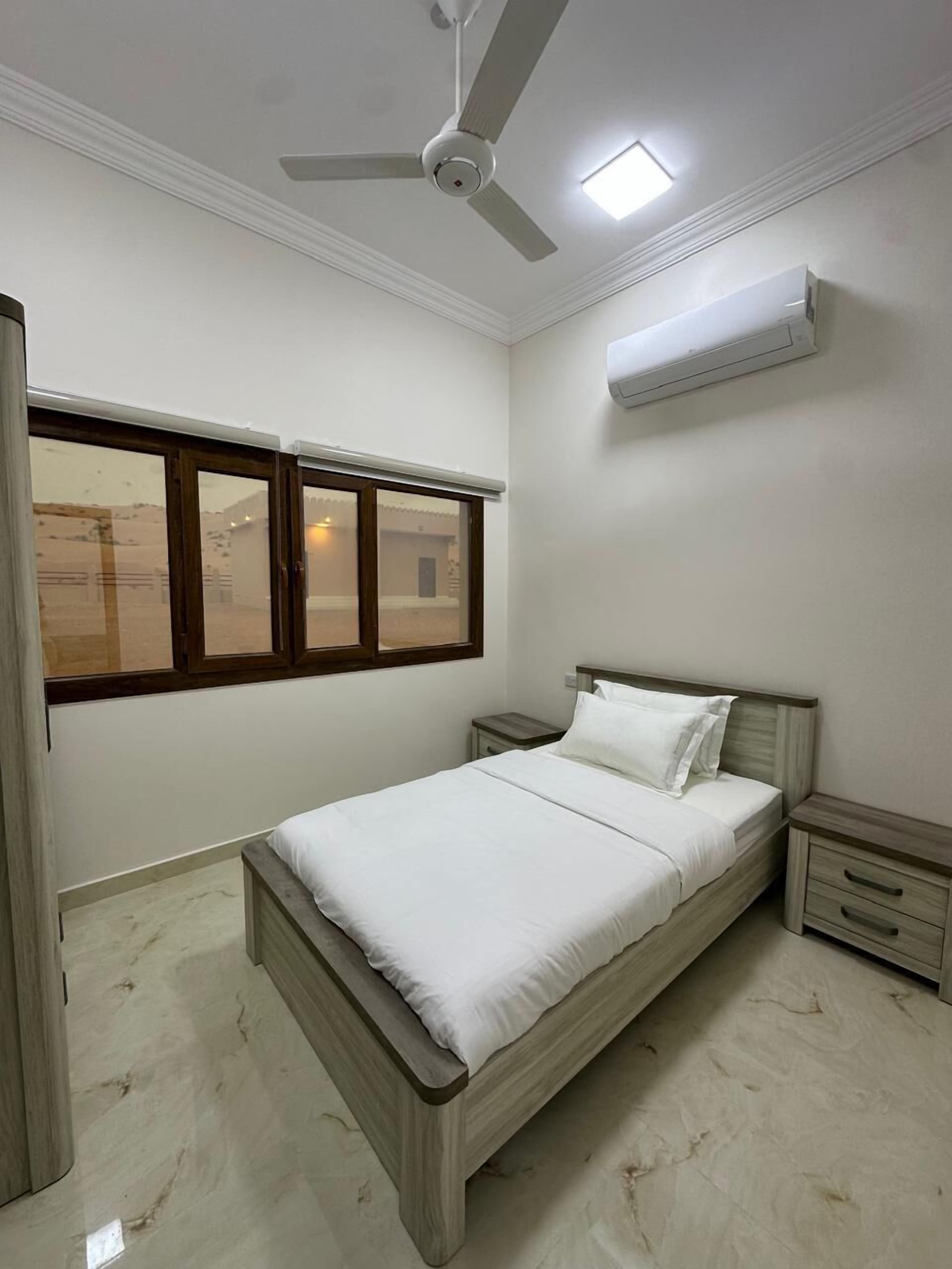 A bedroom with a bed, a nightstand, a ceiling fan, a window, and an air conditioning unit.