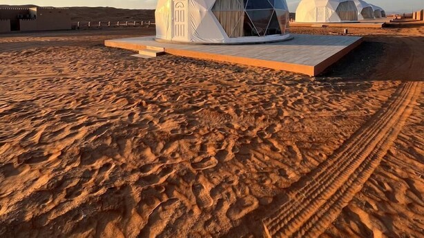 Paisaje desértico con estructuras en forma de cúpulas geodésicas, techos planos y cielo despejado.
