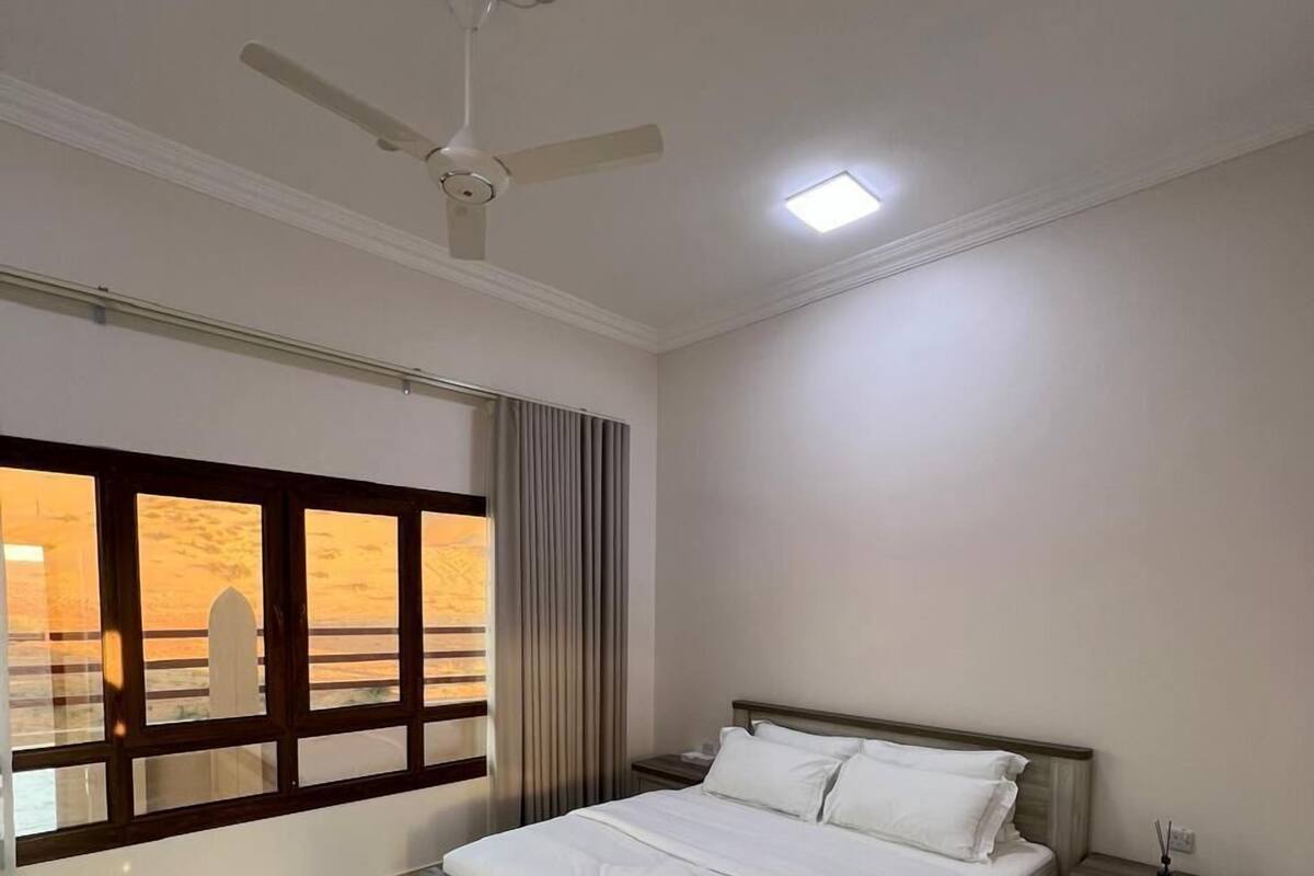 A bedroom with a bed, a nightstand, a ceiling fan, and a window with curtains.