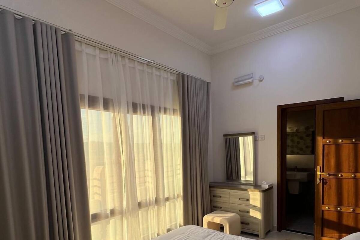 A bedroom with a bed, a dresser, a mirror, and a ceiling fan.