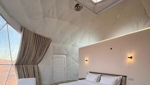 Un dormitorio moderno con una cama grande, una zona de estar con una mesa y vistas a través de una ventana.