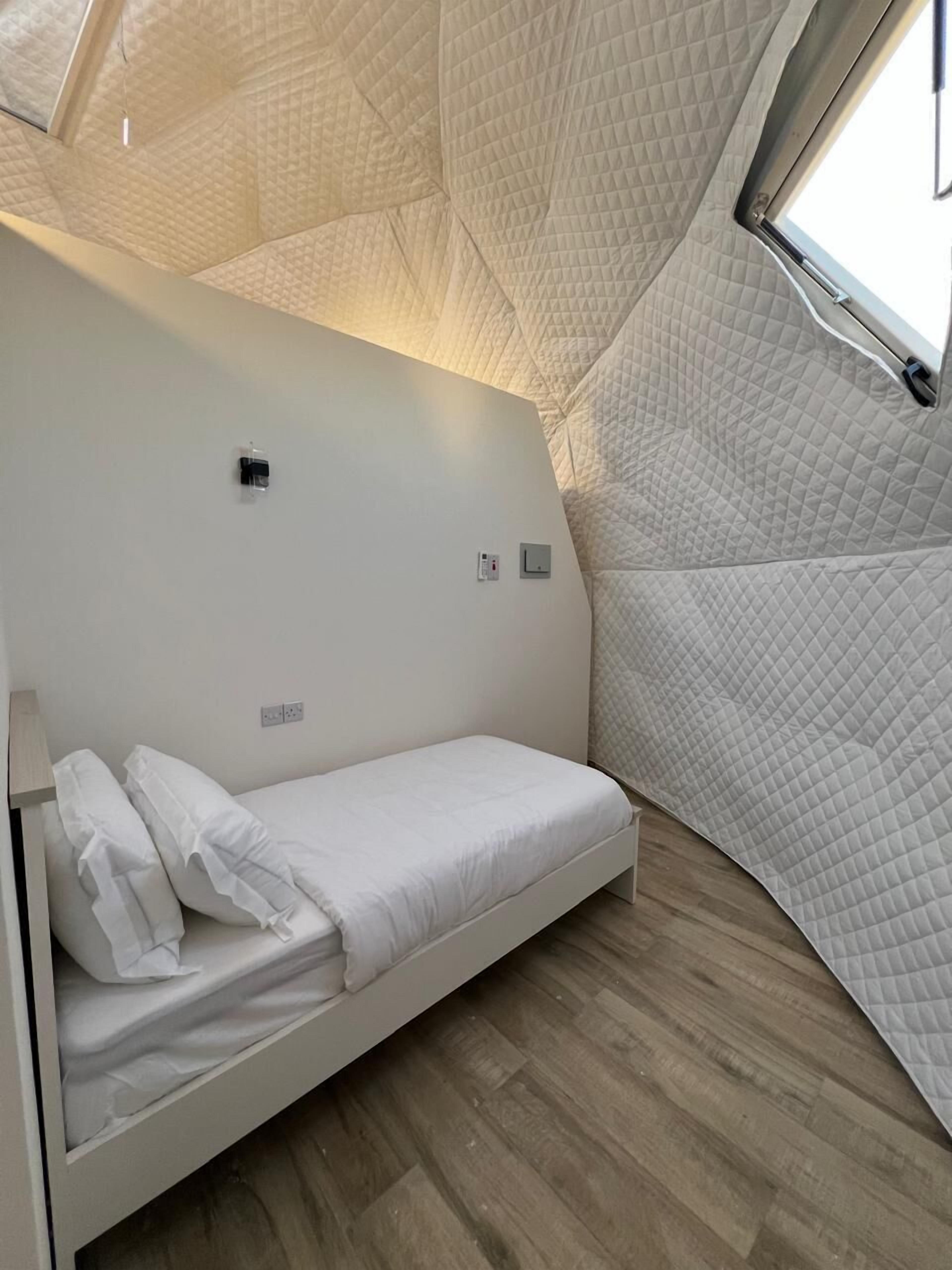 Una habitación compacta y moderna con una cama individual, una ventana pequeña y un diseño original de techo acolchado.