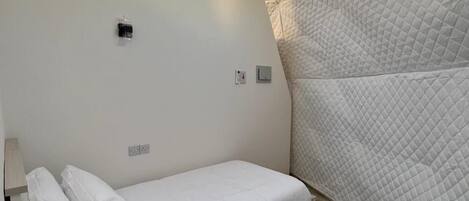 Una habitación compacta y moderna con una cama individual, una ventana pequeña y un diseño original de techo acolchado.