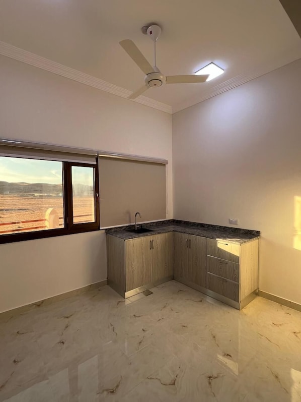 A kitchen with a built-in sink, a ceiling fan, and a window with a view of a desert landscape. - Modern desert gate resort (Bidiya)