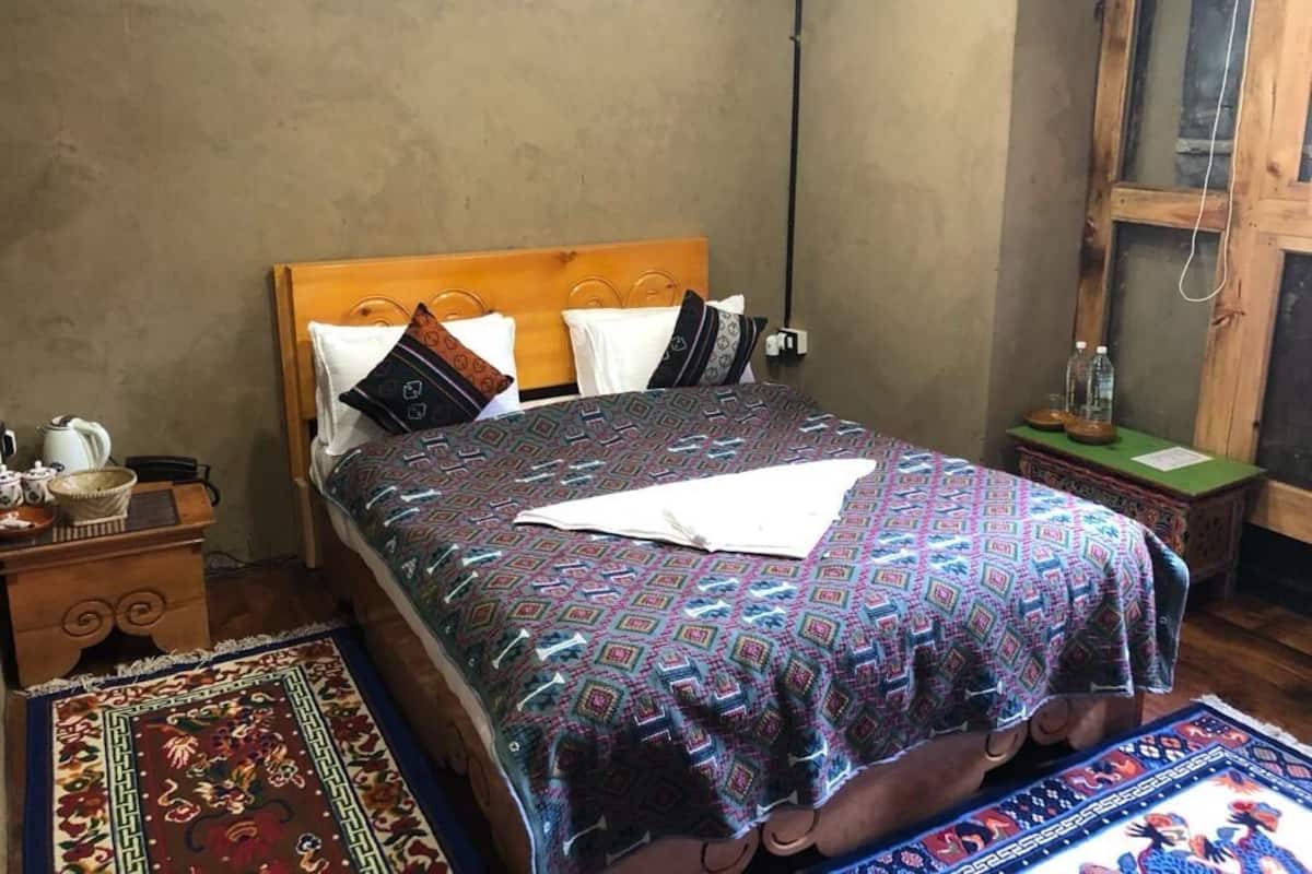 A bed with patterned bedding, a wooden headboard, and a nightstand with a kettle and a basket.