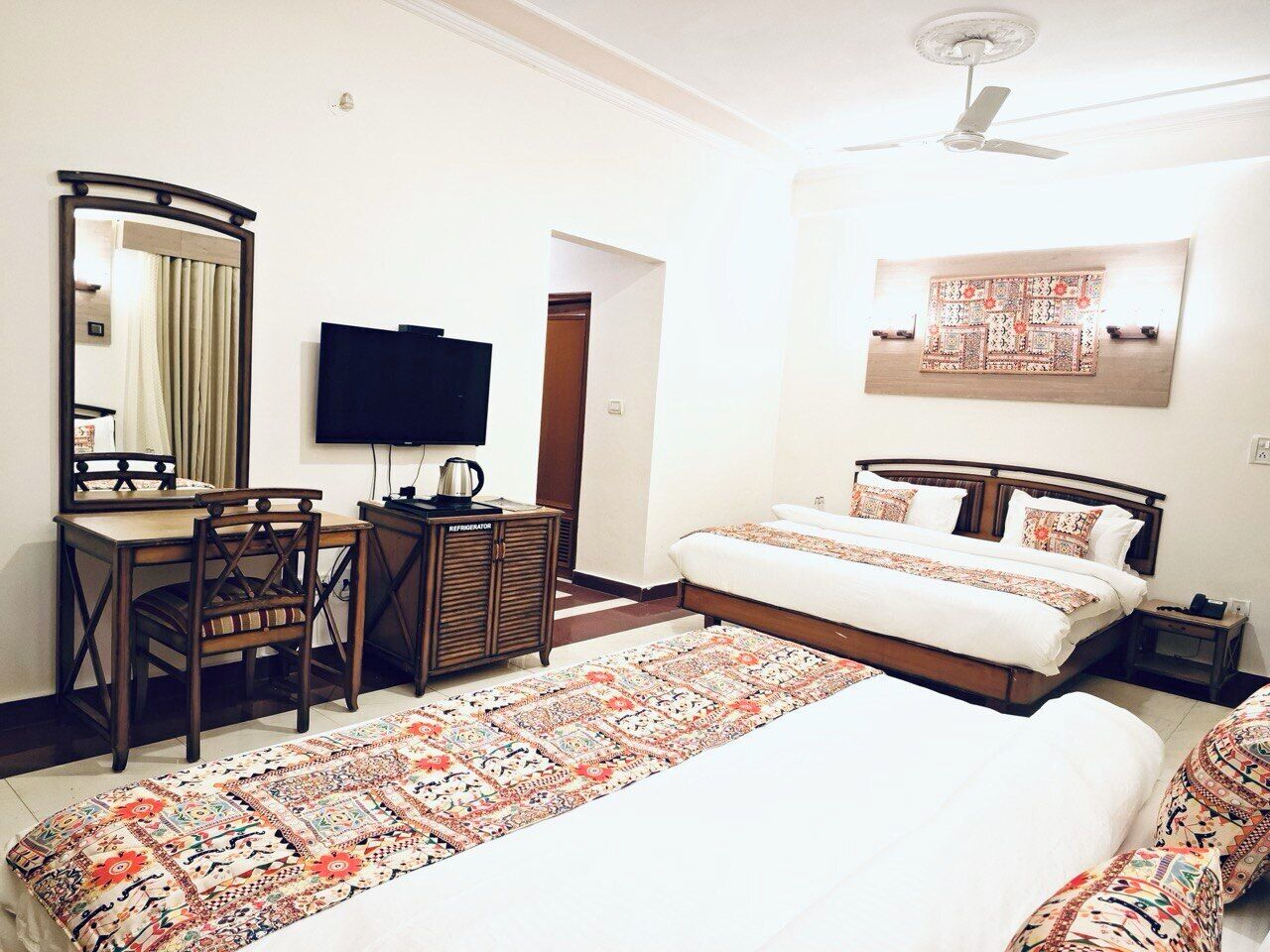 A hotel room with a large bed, a desk with a chair, a television, and a ceiling fan.