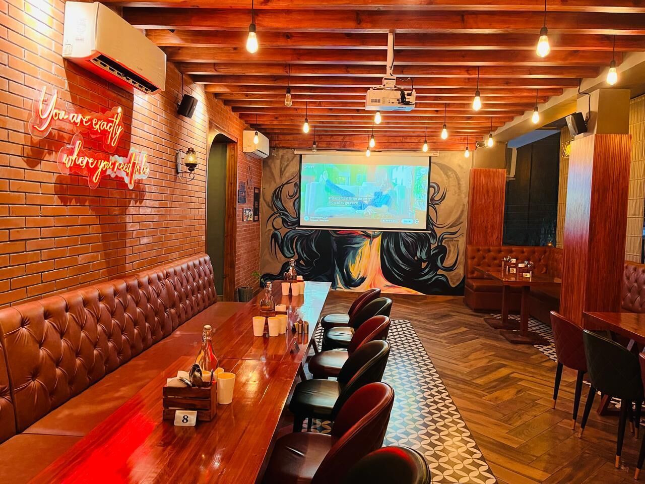 A conference room with a long table, leather seating, a projector screen, and a mural on the wall.