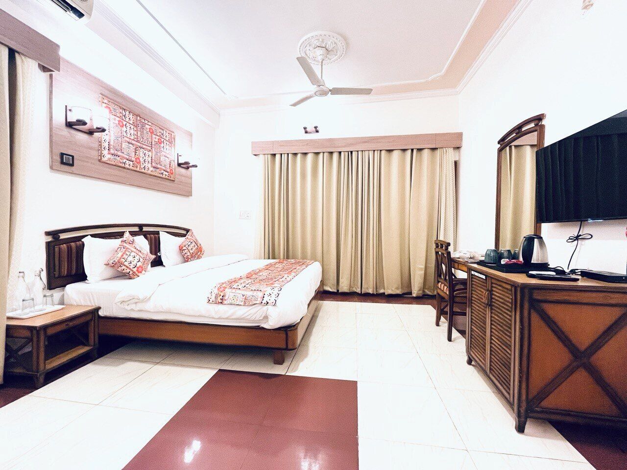A hotel room with a bed, a desk, a chair, a ceiling fan, and a TV.