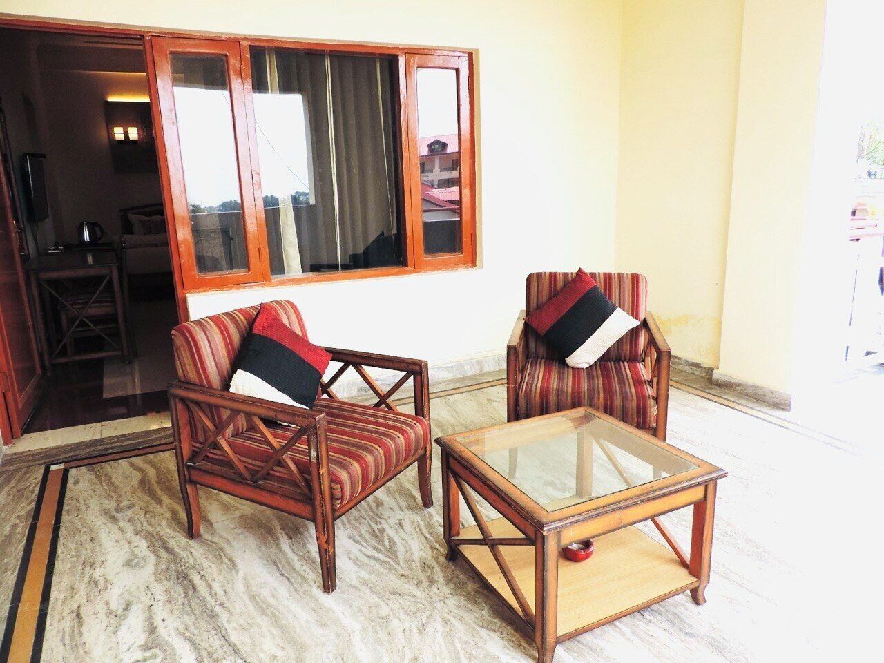 A room with two wooden armchairs with striped upholstery and black cushions, a glass-top coffee table, and a large window with curtains.