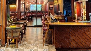 A restaurant interior with wooden paneling, a bar area, and a large screen displaying a movie. - Hotel Palampur Life (Palampur)